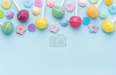 Foto de Coloridas piruletas dulces y caramelos sobre fondo azul. Piso tendido, vista superior - Imagen libre de derechos