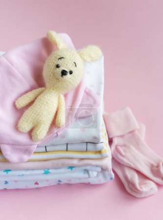 Foto de Pila de trajes de bebé. Juguete de punto de bebé de conejito junto a una pila de mamelucos para niño - Imagen libre de derechos