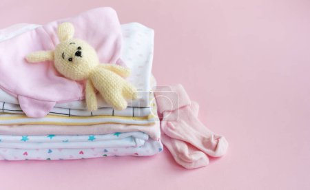Foto de Pila de trajes de bebé. Juguete de punto de bebé de conejito junto a una pila de mamelucos para niño - Imagen libre de derechos