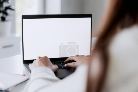 Frau tippt mit leeren leeren weißen Bildschirmattrappen auf dem Laptop. Der Computer liegt auf dem weißen Tisch. Unscharfer Hintergrund. Personen, die von zu Hause aus arbeiten. Leerzeichen für Text kopieren