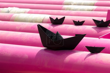 Téléchargez les photos : Bateaux en papier noir naviguent à travers des tuyaux en fer rose. imitation - en image libre de droit