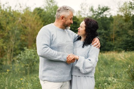 Photo for Close up romantic couple standing in autumn park and hugging in daytime. Man and woman wearing blue sweaters. Woman is brunette and man is gray. - Royalty Free Image
