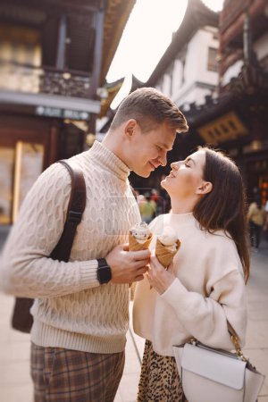 Foto de Pareja recién casada comiendo helado de un cono en una calle de Shanghai cerca de Yuyuan. Pareja tomar un descanso para un aperitivo durante su visita a China. marido y mujer compartiendo helado fuera de una sala de comidas - Imagen libre de derechos