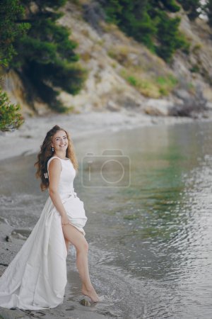 Téléchargez les photos : Belle mariée aux cheveux longs dans une magnifique robe blanche marchant sur une plage - en image libre de droit