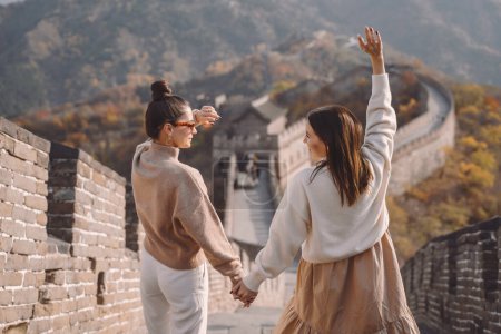 Photo for Two female friends walking along the Great Wall of China near the Beijing entarnce. Two stylish girls exploring chinese culture together. Two girls holding hands dressed in matching outfits. - Royalty Free Image