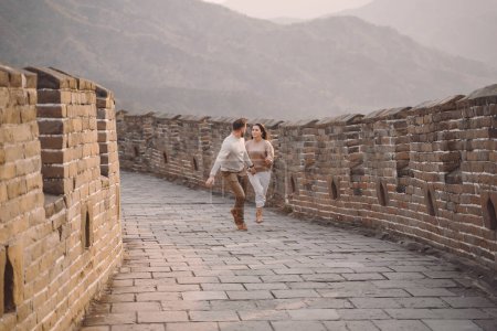 Foto de Pareja joven corriendo y girando en la Gran Muralla de China. Pareja recién casada en su luna de miel con la Gran Muralla China cerca de Beijing China
. - Imagen libre de derechos