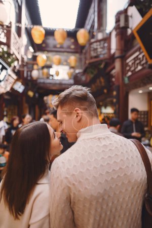 Foto de Recién casados mostrando afecto en Shanghai cerca de Yuyuan. Pareja tomar un descanso para algunos abrazos durante su visita a China. marido y mujer tomados de la mano en la calle por un mercado y pagoda - Imagen libre de derechos