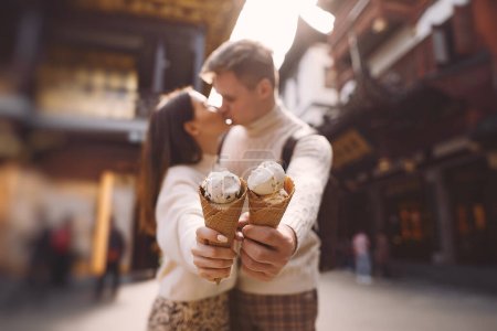 Foto de Pareja recién casada comiendo helado de un cono en una calle de Shanghai cerca de Yuyuan. Pareja tomar un descanso para un aperitivo durante su visita a China. marido y mujer compartiendo helado fuera de una sala de comidas - Imagen libre de derechos