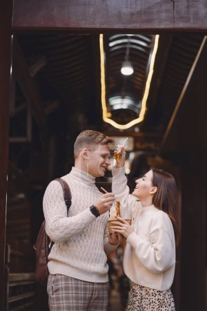 Photo for Newlywed couple eating noodles with chopsticks in Shanghai outside a food market near Yuyuan. Couple eating authentic local food. husband and wife eating chinese food outisde of a food hall - Royalty Free Image