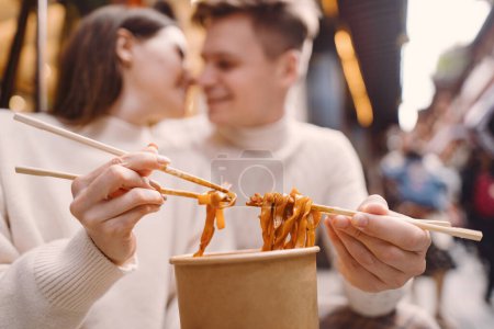Foto de Pareja recién casada comiendo fideos con palillos en Shanghai fuera de un mercado de alimentos cerca de Yuyuan. Pareja comiendo auténtica comida local. marido y mujer comiendo comida china fuera de una sala de comida - Imagen libre de derechos