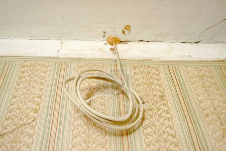 Foto de Un cable enrollado cuelga del techo. El cable se enrolla debajo del techo. Renovación en la casa. - Imagen libre de derechos