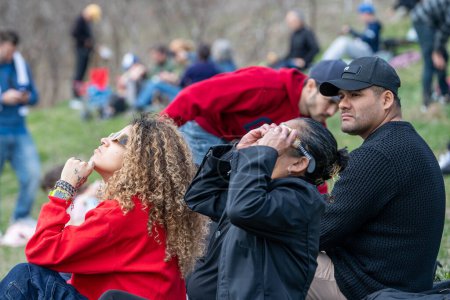 Foto de Toronto, Canadá - 8 de abril de 2024: La gente ve el comienzo del eclipse solar parcial en Riverdale Park, usando sus gafas de eclipse especiales. - Imagen libre de derechos
