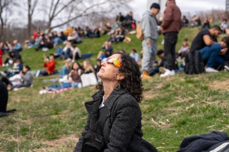 Téléchargez les photos : Toronto, Canada - 8 avril 2024 : Une femme observe le début de l'éclipse solaire partielle au parc Riverdale, portant des lunettes spéciales pour l'éclipse. - en image libre de droit
