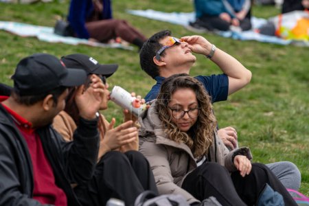 Foto de Toronto, Canadá - 8 de abril de 2024: La gente ve el comienzo del eclipse solar parcial en Riverdale Park, usando sus gafas de eclipse especiales. - Imagen libre de derechos