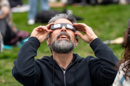 Téléchargez les photos : Toronto, Canada - 8 avril 2024 : Un homme observe le début de l "éclipse solaire partielle au parc Riverdale, portant des lunettes spéciales d" éclipse. - en image libre de droit