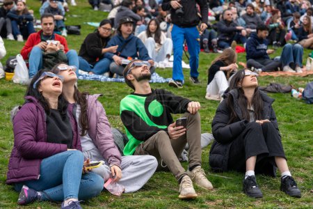 Photo for Toronto, Canada - April 8, 2024: People watch the beginning of the partial solar eclipse at Riverdale Park, wearing their special eclipse glasses. - Royalty Free Image