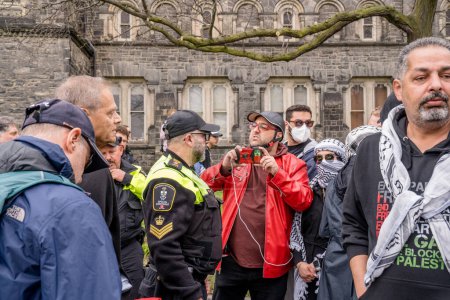 Photo for Pro-Palestinian students form a human chain, preventing Pro-Israel protesters from crossing, outside the encampment which students created by occupying King College Circle at University of Toronto. - Royalty Free Image