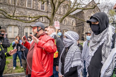 Foto de Estudiantes pro-palestinos enmascarados forman una cadena humana, impidiendo que los manifestantes pro-Israel crucen, fuera del campamento que los estudiantes crearon al ocupar King College Circle en la Universidad de Toronto. - Imagen libre de derechos
