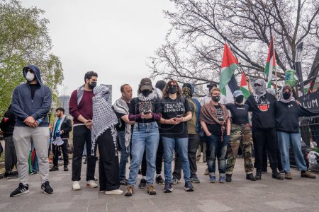 Téléchargez les photos : Les étudiants pro-palestiniens masqués forment une chaîne humaine, empêchant les manifestants pro-israéliens de traverser, à l'extérieur du campement que les étudiants ont créé en occupant le King College Circle à l'Université de Toronto. - en image libre de droit
