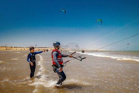 Téléchargez les photos : Essaouira, Maroc - 3 août 2023 : Un moniteur de kitesurf apprend à un homme à manœuvrer le cerf-volant sur la plage. L'endroit est réputé pour les amateurs de kitesurf, grâce au vent fort, toujours présent, qui vous permet de soulever facilement le cerf-volant en vol. - en image libre de droit