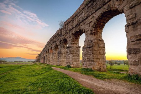 Foto de Arcos de un antiguo acueducto romano, hecho de bloques de toba. Un sendero corre a lo largo de la propiedad en un parque verde en las afueras de Roma
. - Imagen libre de derechos