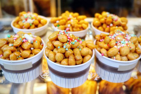 Cups filled with Struffoli, typical Neapolitan pastry consisting of many small balls of dough fried in oil and wrapped in warm honey. Decorated with colored sprinkles.