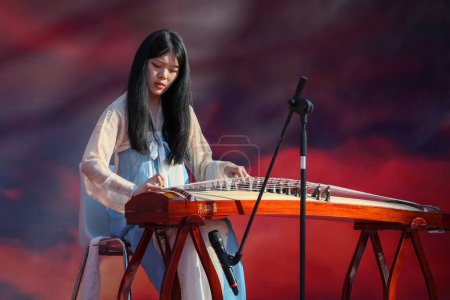 Photo for Rome, Italy - February 18, 2024: Chinese New Year celebrations in the square, public event. Chinese girl plays the Guzheng, traditional Chinese bowed zither, during musical performance on stage. - Royalty Free Image