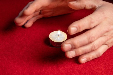 Téléchargez les photos : Hands warming themselves on a tealight, red background. High quality photo - en image libre de droit