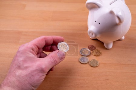 Foto de Piggy bank with male hand and some Euro coins. High quality photo - Imagen libre de derechos