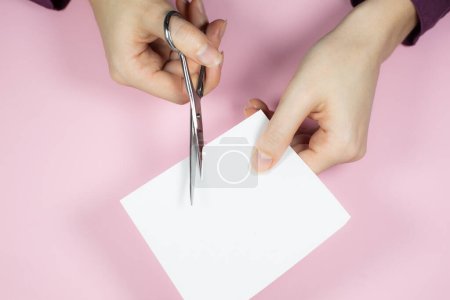 Woman is cutting white paper with scissors, close up.