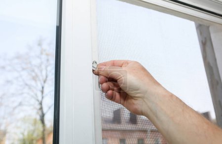 Foto de Man is installing the mosquito net on the window. Protection from bugs. - Imagen libre de derechos