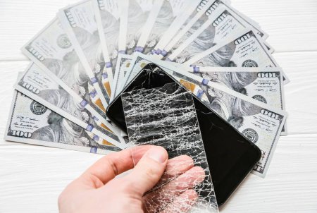 Photo for Man is holding broken screen protector tempered glass. Money lying near the phone. Dollar notes. - Royalty Free Image