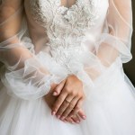 Bride is holding her hands on waist. Beautiful long sleeve dress. Lace cloth. Wedding morning details.