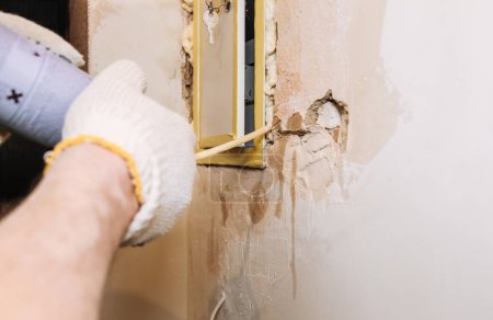 Photo for Worker is filling spray foam near electrical panel. Maintenance repair works renovation in the flat. Restoration indoors. - Royalty Free Image