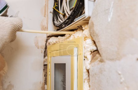 Photo for Worker is filling spray foam near electrical panel. Maintenance repair works renovation in the flat. Restoration indoors. - Royalty Free Image