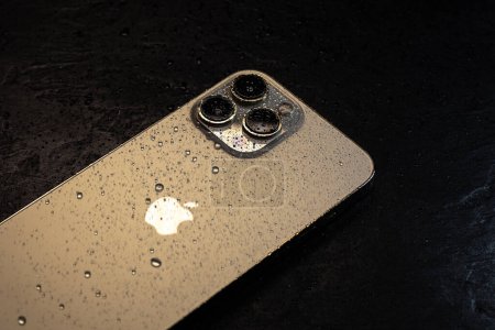 Foto de KYIV, UCRANIA - 20 de octubre de 2023: smartphone moderno Apple iPhone 15 Pro con gotas de agua sobre fondo negro. Tecnología moderna resistente al agua. - Imagen libre de derechos