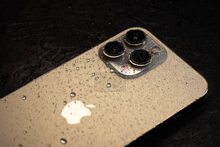 Foto de KYIV, UCRANIA - 20 de octubre de 2023: smartphone moderno Apple iPhone 15 Pro con gotas de agua sobre fondo negro. Tecnología moderna resistente al agua. - Imagen libre de derechos