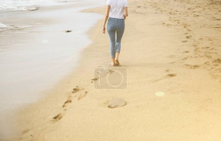 Foto de Hipster chica está caminando en la playa.Hermosa vista al mar. Grandes olas en la orilla del mar. Línea costera con huellas. Vacaciones de verano. Concepto de viaje. - Imagen libre de derechos