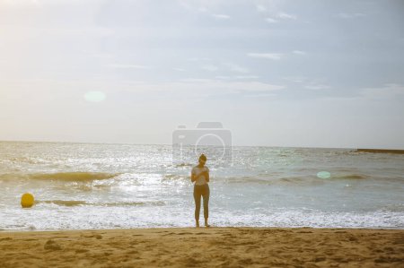Foto de Hipster chica está buscando en el teléfono en la playa. Grandes olas en el lado del océano. Costera en las nubes y el sol. Vacaciones de verano. Concepto de viaje. - Imagen libre de derechos