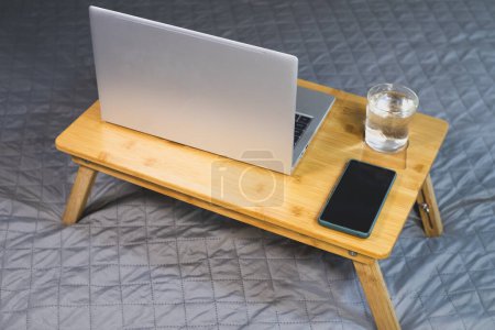 Laptop, smartphone y vaso de agua en la almohadilla de enfriamiento de madera para portátil. Enfriador portátil para computadora, ventilador USB.