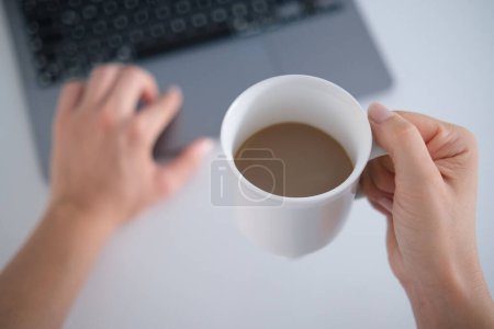 Foto de Imagen de maqueta de vista superior de una mujer de negocios sosteniendo café con leche mientras usa el portátil en la mesa blanca.. - Imagen libre de derechos