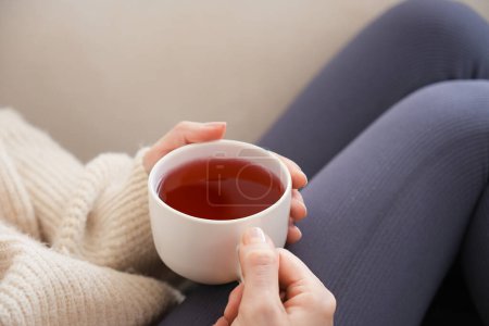 Foto de Vista lateral mujer joven sosteniendo una taza de té de hierbas blanco.Mujer joven sentada en un sofá blanco mimándose en casa en un día de invierno. - Imagen libre de derechos