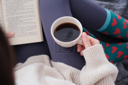 Foto de Vista superior de la joven morena con café y libro en mano.Horas pacíficas en casa con libro y café. - Imagen libre de derechos