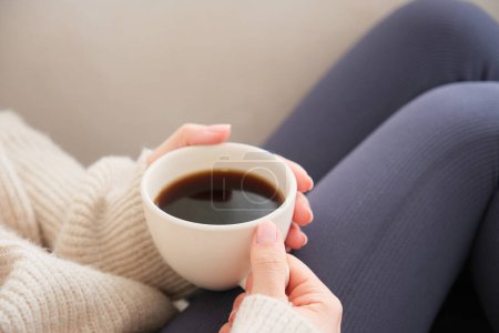 Foto de Vista lateral de la joven mujer sosteniendo taza de café en la mano sentado en el sofá blanco.Pase tiempo en casa, tome un breve descanso en casa. - Imagen libre de derechos