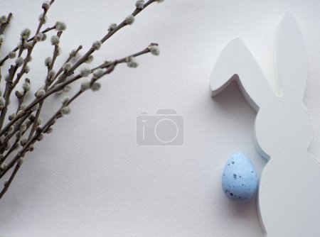 Happy Easter, white concept. Easter decorations on white background with copy space. Easter greating card. Flat lay. Willow twigs, blue egg and white bunny. Celebrating Easter holidays.