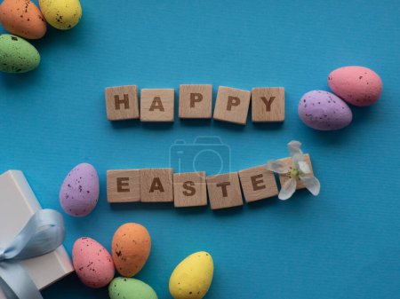 Photo for Happy Easter concept. Easter decorations on blue background with copy space. Easter greating card. Flat lay. Colorful eggs and white gift box. Buying gifts for the Easter holidays. - Royalty Free Image
