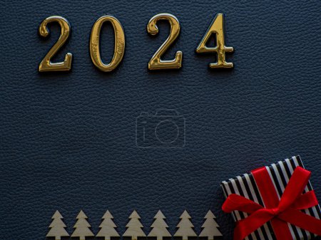 Téléchargez les photos : 2023 sur fond sombre. Les figurines en or 2023 se trouvent près d'un petit cadeau dans un emballage noir et blanc dépouillé et avec des rubans rouges et des sapins en bois sur le carton foncé. Carte de Noël et Nouvel An. - en image libre de droit