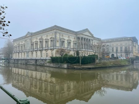 The Palace of Justice in Ghent Belgium. Stunning building with neoclassical and Gothic revival styles. Completed in 1846, popular tourist attraction. Historic building reflecting in canal on misty day
