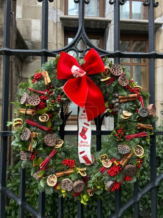 A stunning christmas wreath adorned with vibrant red and green decorations hangs gracefully on an elegant metal gate, creating a perfect holiday scene.