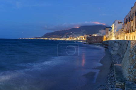 Téléchargez les photos : Une belle petite ville balnéaire éclairée la nuit, construite juste à côté d'une mer calme. - en image libre de droit